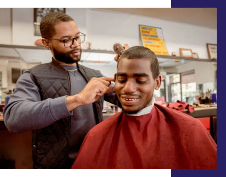A Black man giving a haircut to a Black man at a B.A.R.B.E.R.S.H.O.P. event.