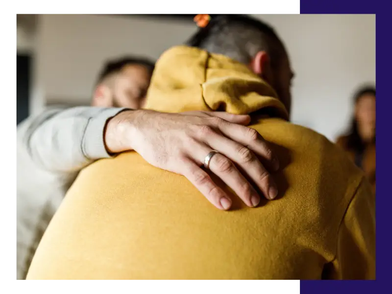 A man puts his arm around another man in a show of support during group therapy.