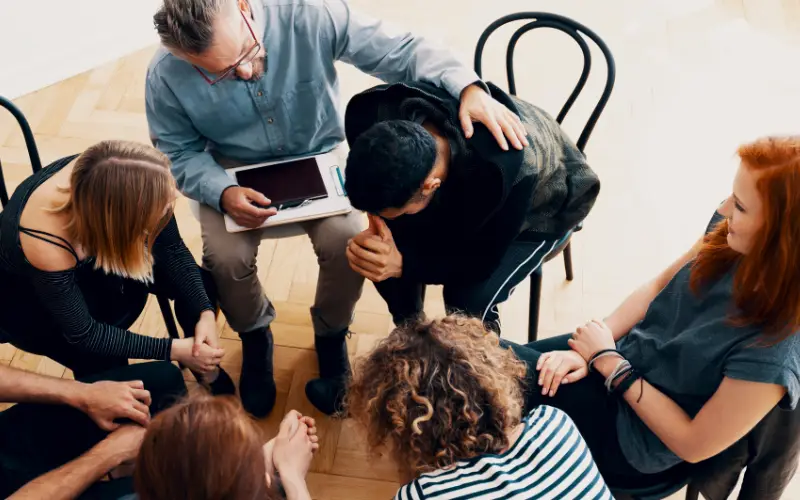A therapist comforts a young person in distress during a group therapy session, looking from above.
