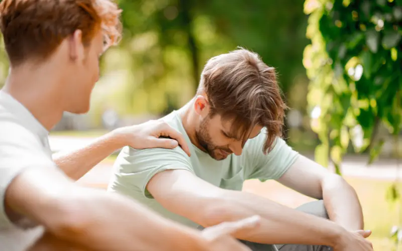 A young White man comforts another young White man in a show of support.