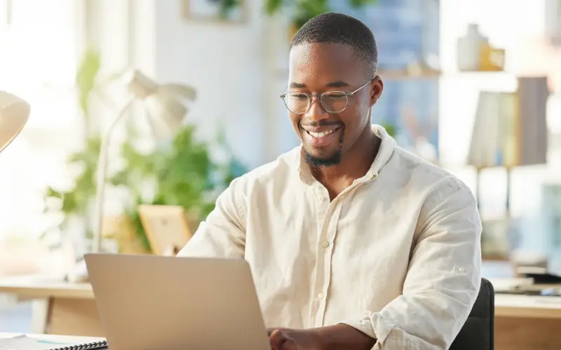 A young Black professional uses a laptop and appears happy and confident.