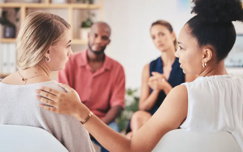 A woman supports another woman during a group therapy session.