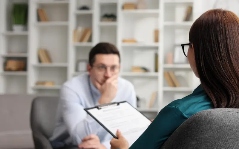 A man talks to a women therapist with a clipboard.
