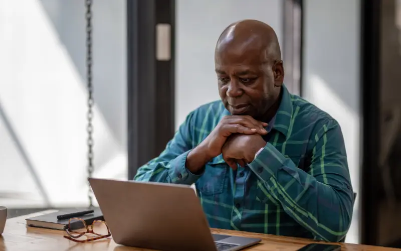 An older Black man uses a laptop to search for information.