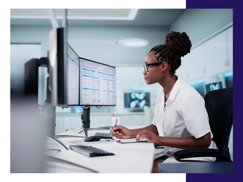A Black woman with glasses studying data trends on a computer.